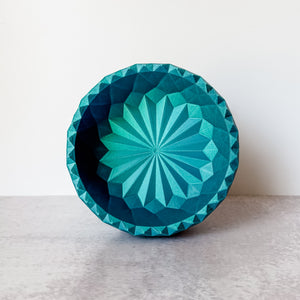 Geometric teal bowl on a light gray surface with a white background