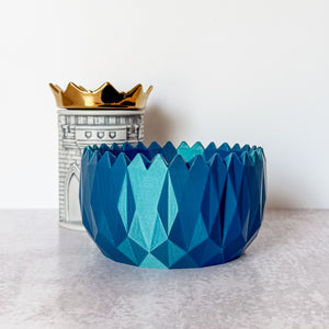Blue geometric-patterned vase with a gold crown on a white surface