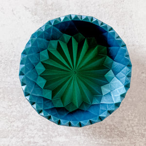 Geometric blue and green patterned object on a textured white background