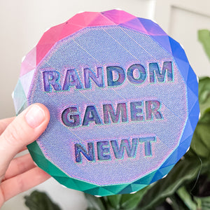Round, multicolored object with 'RANDOM GAMER NEWT' text held by a hand.